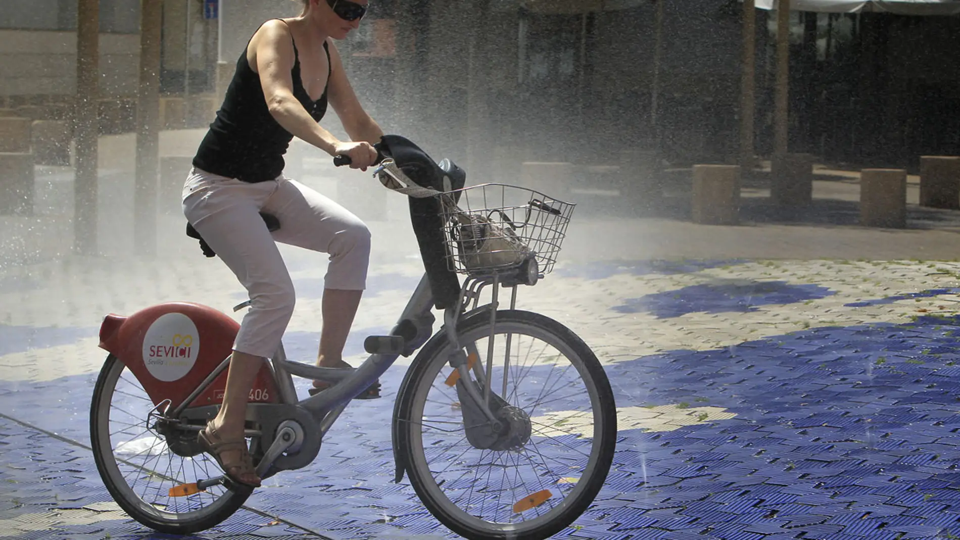 Una joven se refresca en una fuente subida en una bicicleta