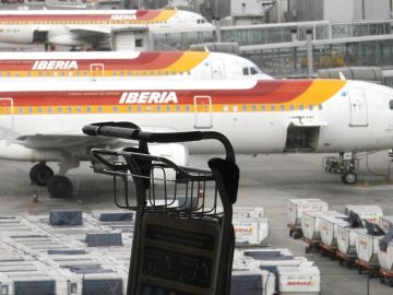 Un carrito de equipajes ante varios aviones de Iberia Un carrito de equipajes ante varios aviones de Iberia