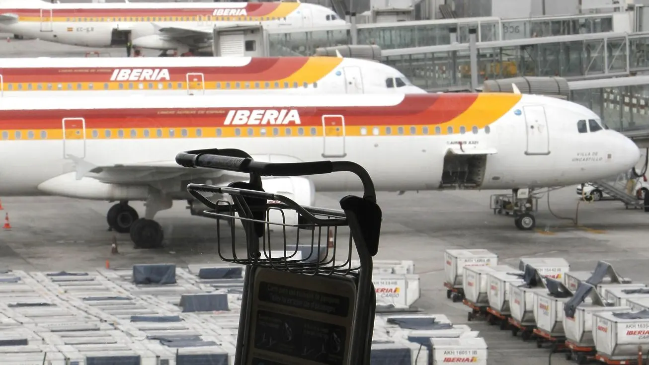 Un carrito de equipajes ante varios aviones de Iberia