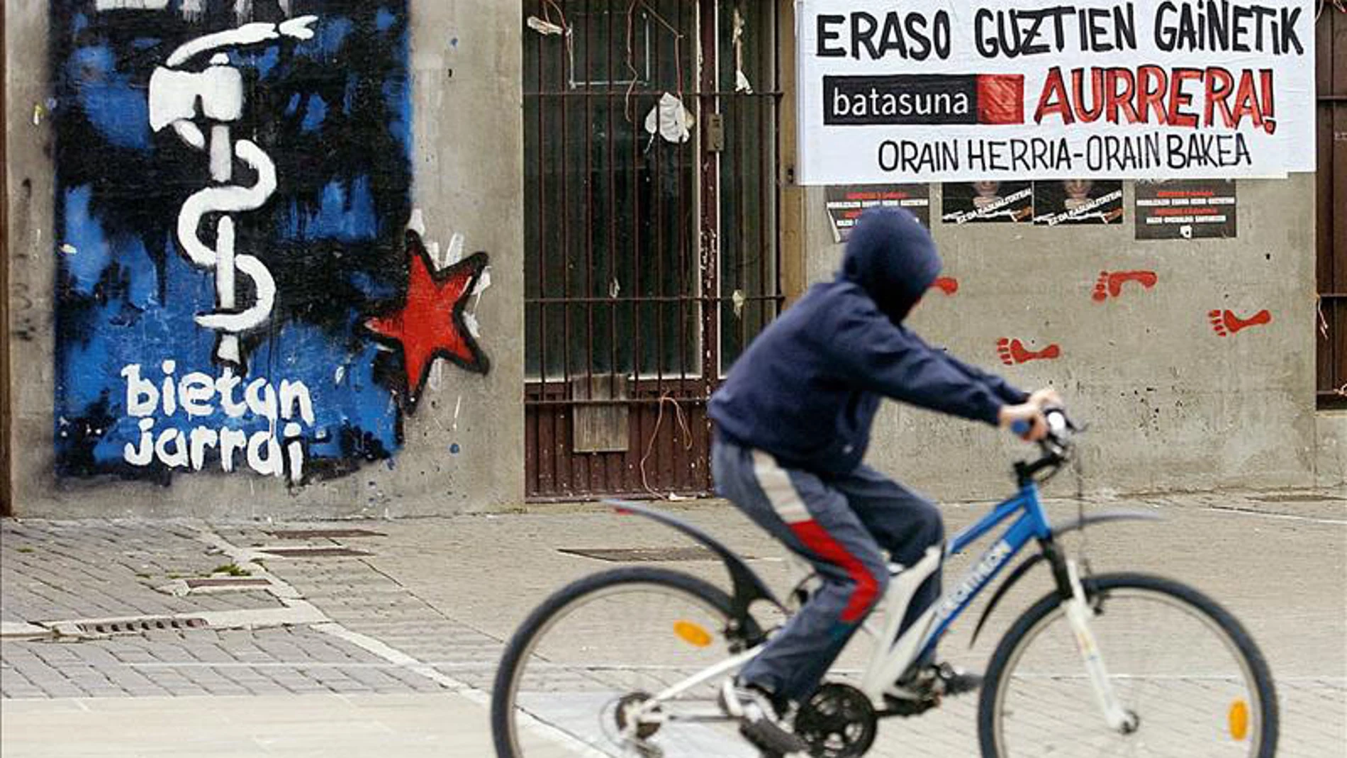 Un joven pasa con su bicicleta por delante de una pintada con el logotipo de ETA 