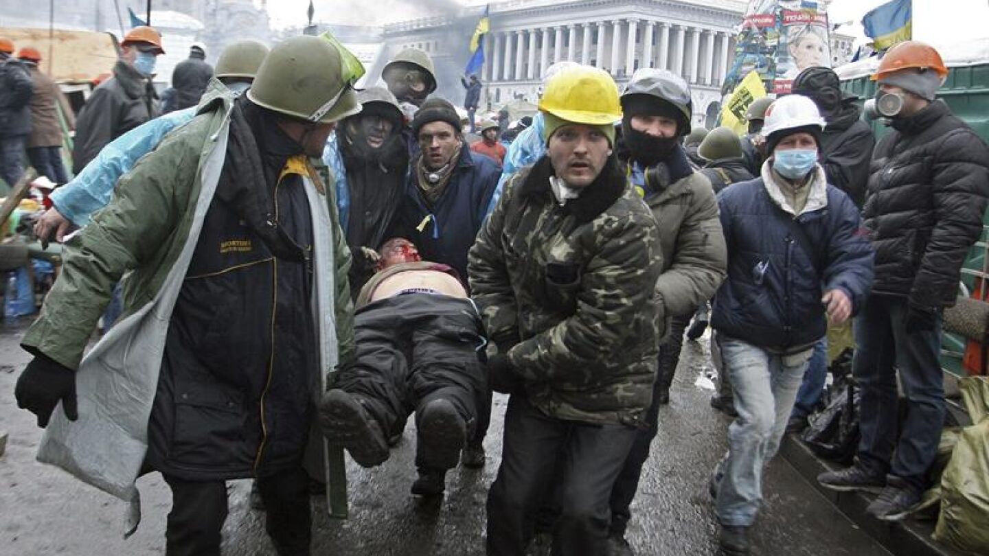 Manifestantes trasladan a un compa&ntilde;ero herido durante los enfrentamientos con los antidisturbios en la Plaza de la Independencia