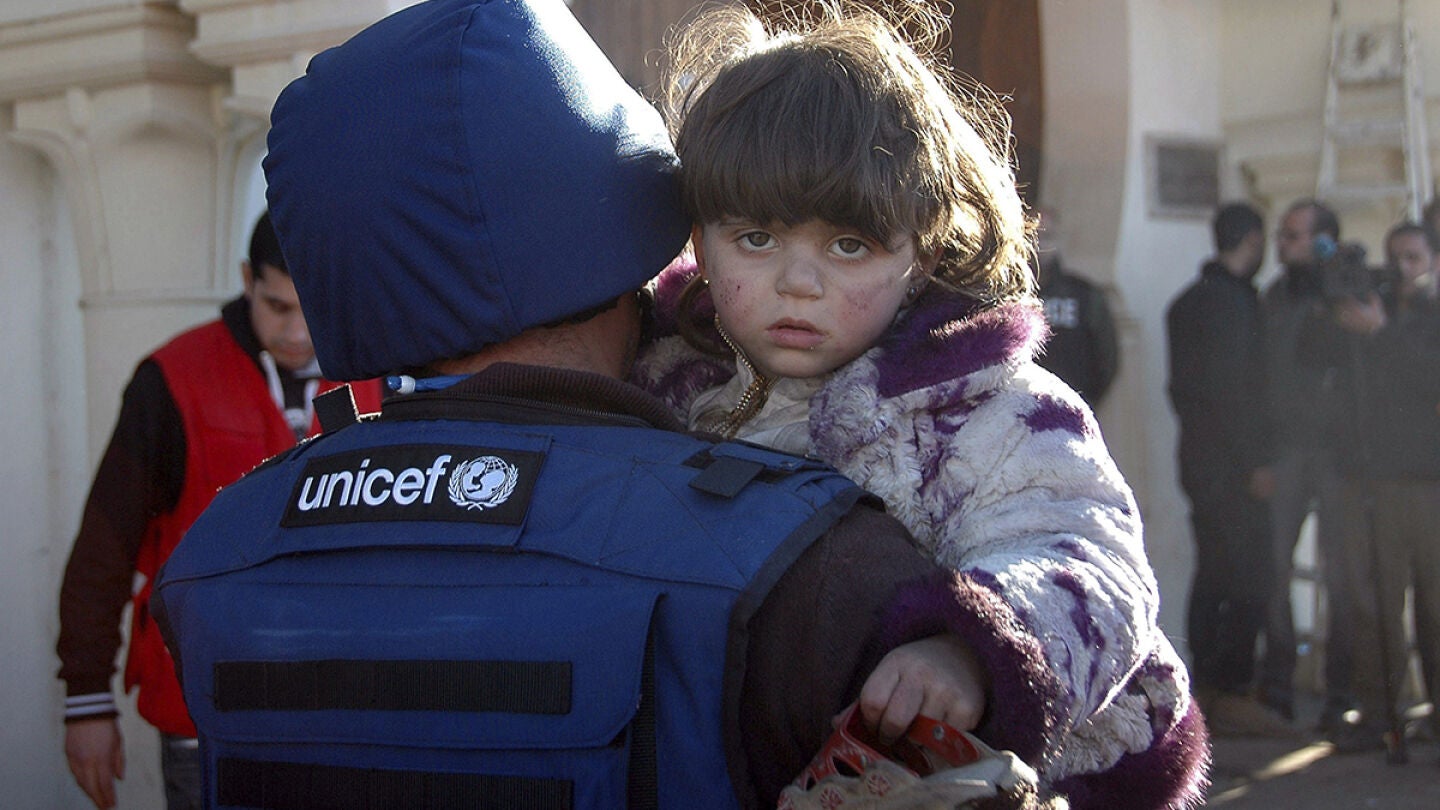 Un miembro de UNICEF lleva en brazos a una ni&ntilde;a siria en un refugio situado en la ciudad de Homs
