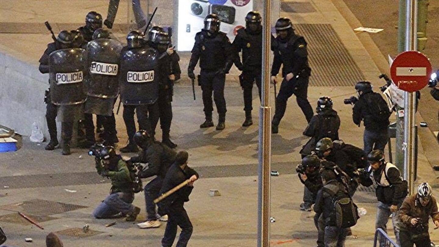  Un joven con un palo ante diversos agentes antidisturbios en las inmediaciones de la Plaza de Col&oacute;n