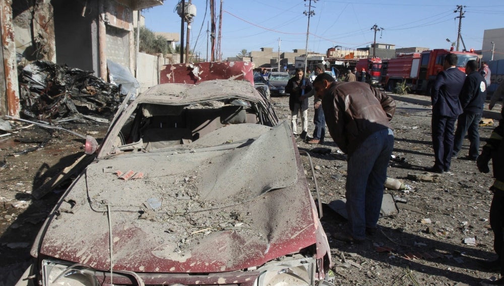 Un grupo de personas inspecciona  un coche bomba en Irak