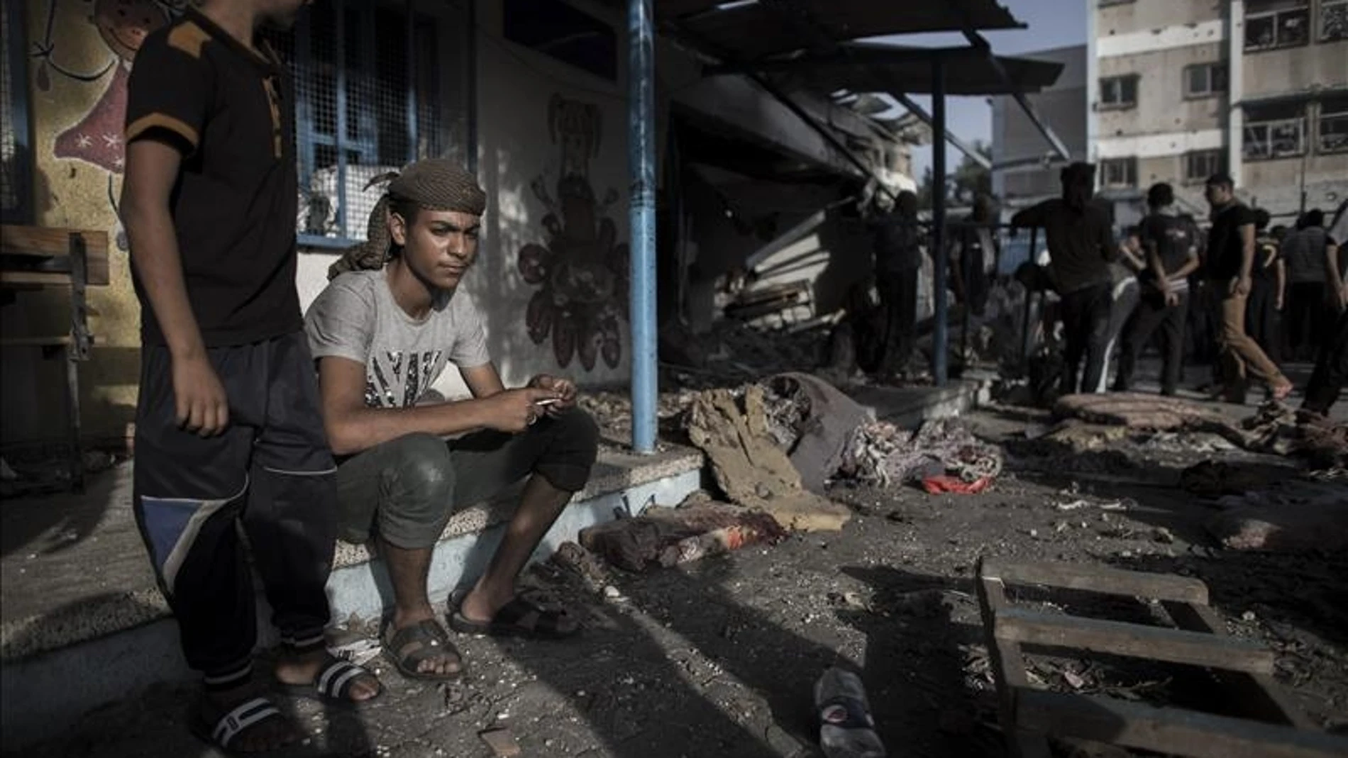 Jóvenes palestinos sentados junto a un aula destruida