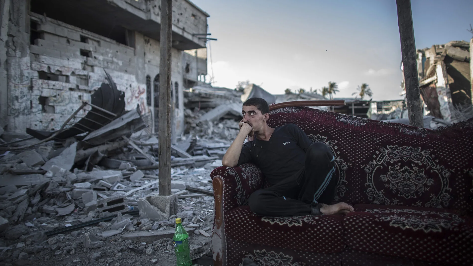 Un palestino descansa sentado en un sofá a la entrada de su casa