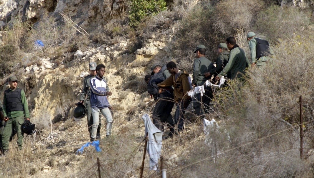 Vista de algunos inmigrantes, con las fuerzas de seguridad en Marruecos, junto a la valla de Melilla