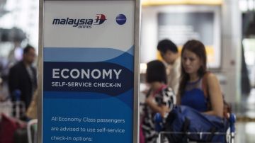 Algunos pasajeros esperan en un mostrador de Malaysia Airlines.
