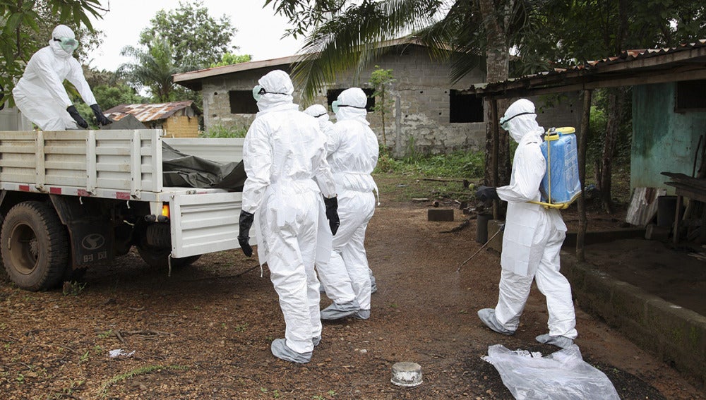 Varios enfermeros liberianos mientras rocían con desinfectante una casa