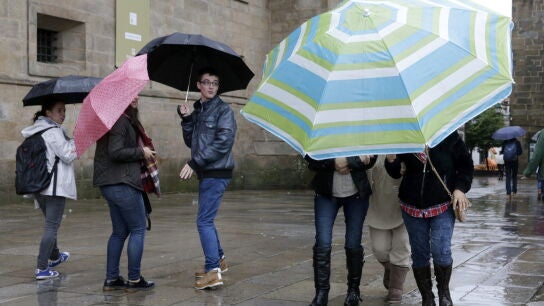 Tres turistas se protegen de la intensa lluvia con una sombrilla en Santiago de Compostela