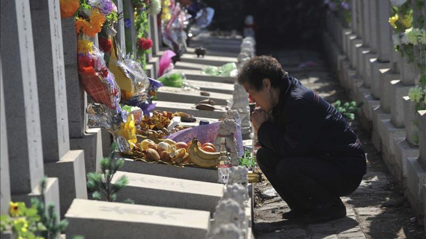 Una mujer reza junto a la tumba de un familiar en un cementerio.