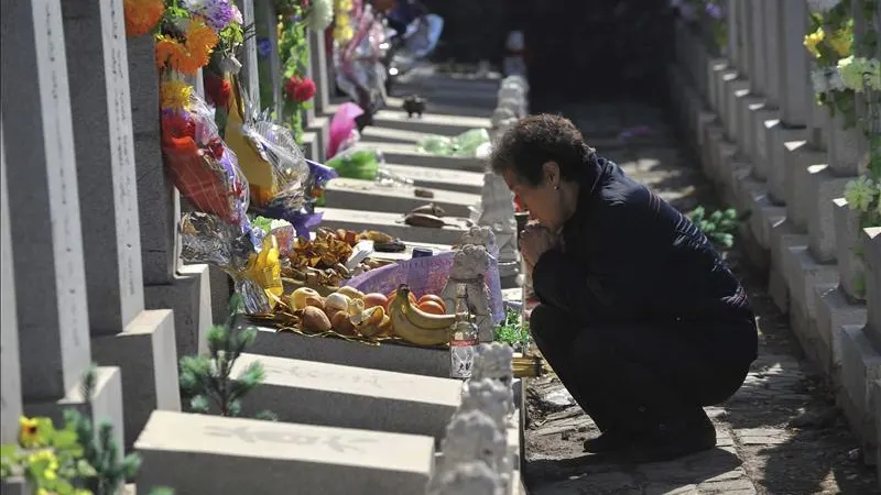 Una mujer reza junto a la tumba de un familiar en un cementerio.
