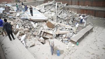 Personas caminando sobre las ruinas de un edificio caído durante el terremoto
