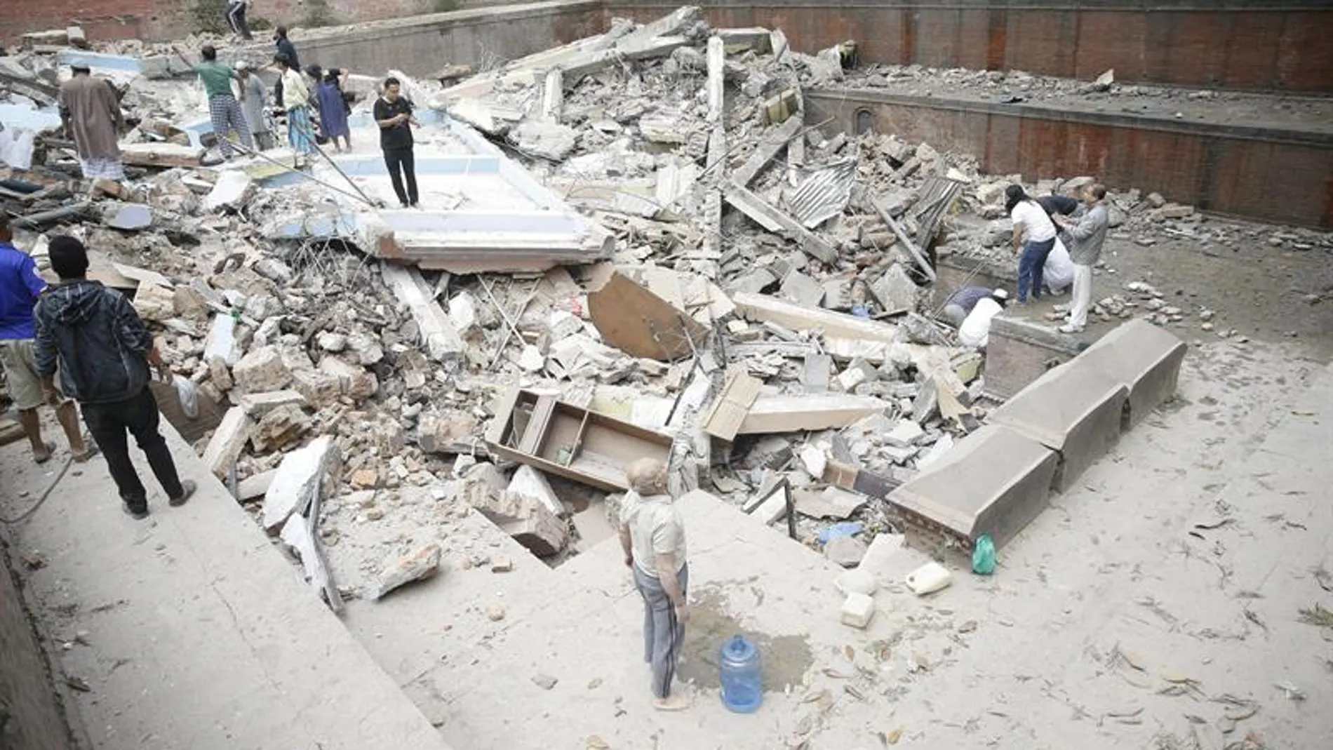 Personas caminando sobre las ruinas de un edificio caído durante el terremoto