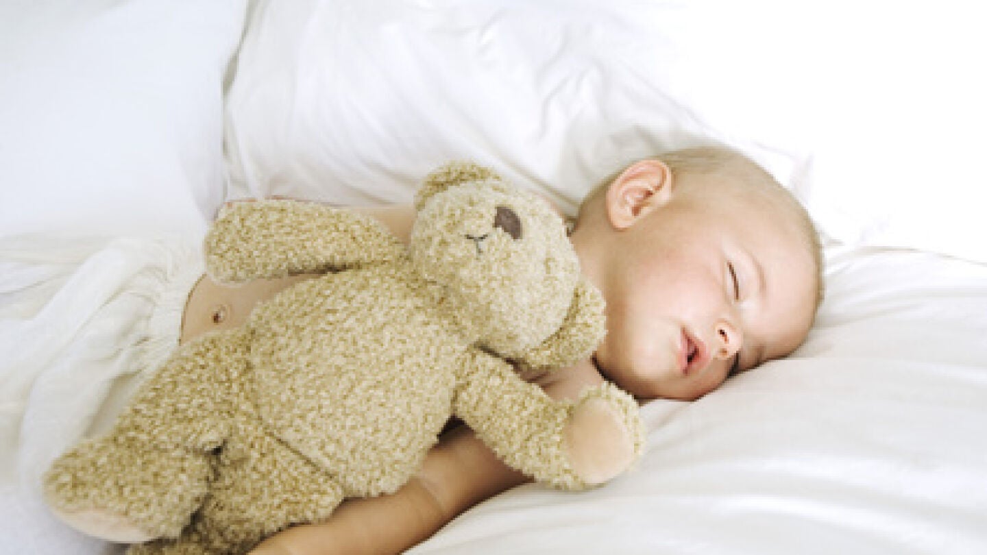 Un beb&eacute; dormido junto a un osito de peluche.