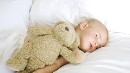 Un bebé dormido junto a un osito de peluche.