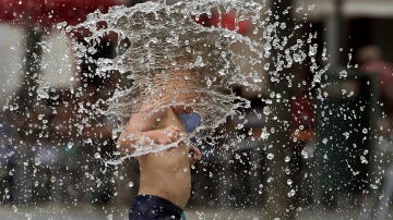 Un niño se refresca en una fuente