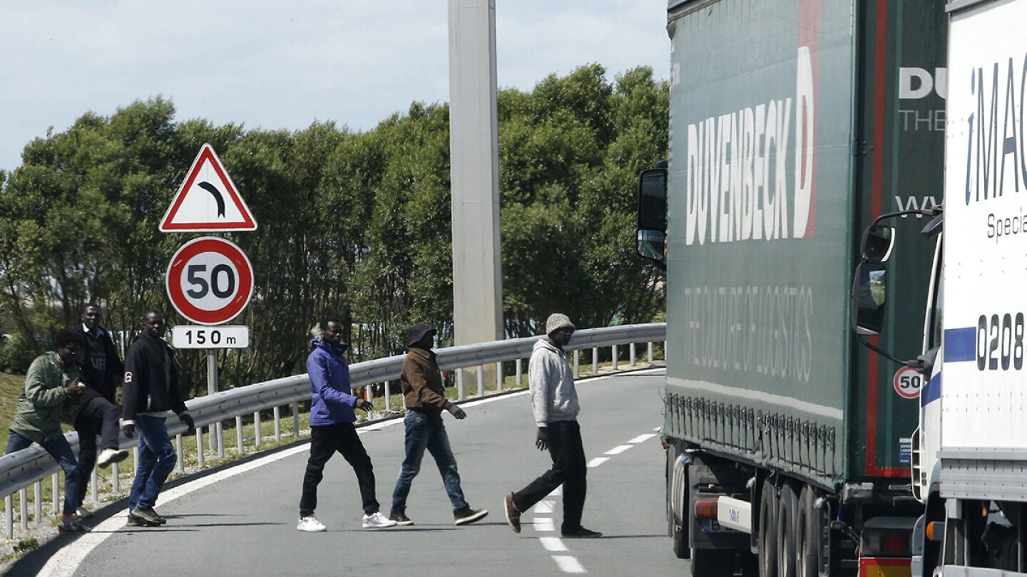 Varios inmigrantes cruzan una carretera cerca de la entrada del Eurot&uacute;nel