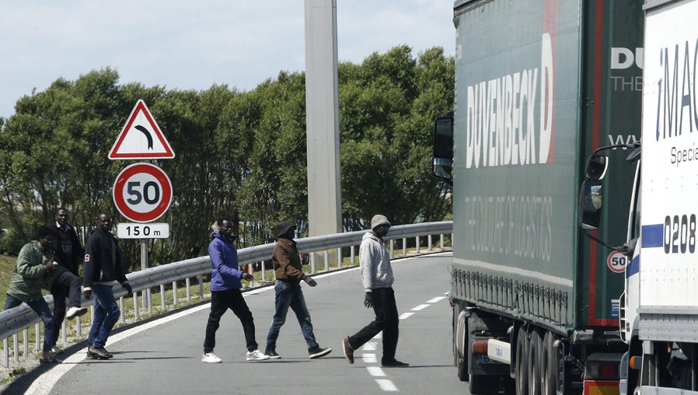 Varios inmigrantes cruzan una carretera cerca de la entrada del Eurotúnel