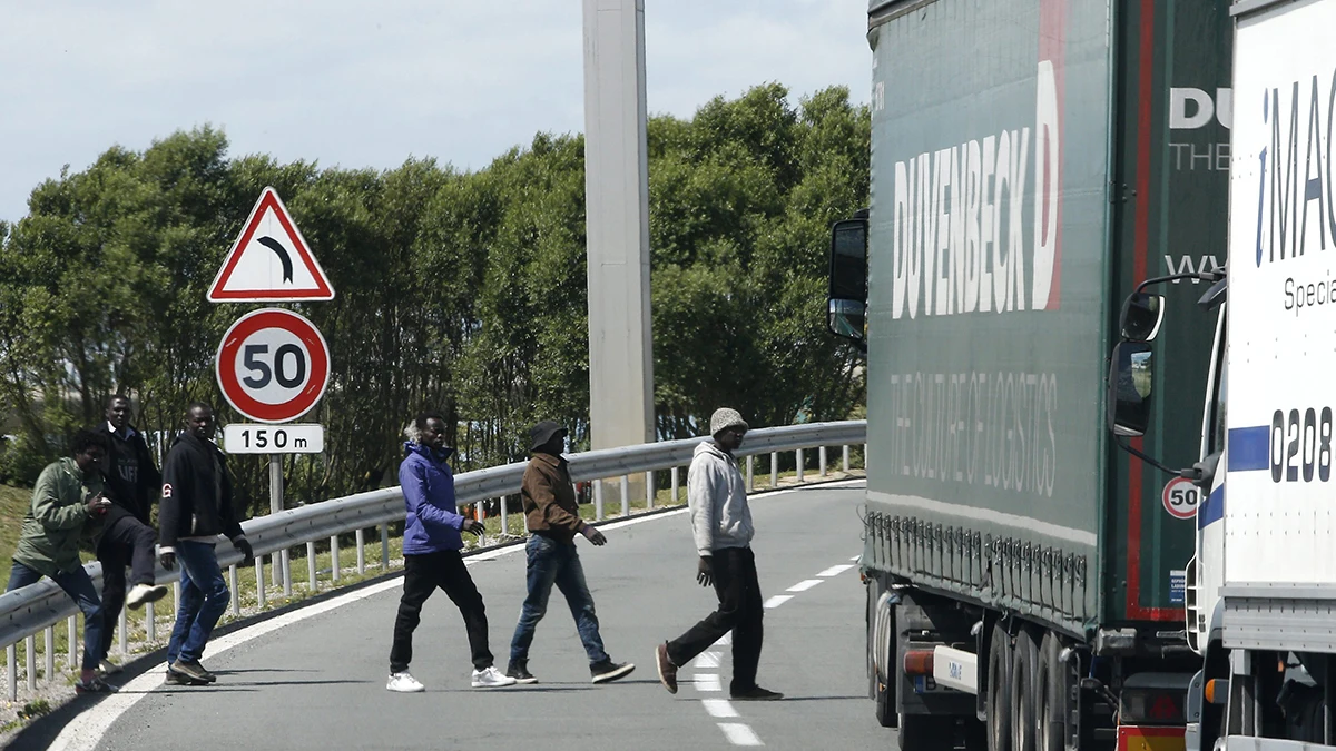 Varios inmigrantes cruzan una carretera cerca de la entrada del Eurotúnel Varios inmigrantes cruzan una carretera cerca de la entrada del Eurotúnel