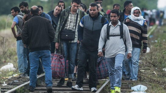 Inmigrantes caminan sobre las v&iacute;as de un tren