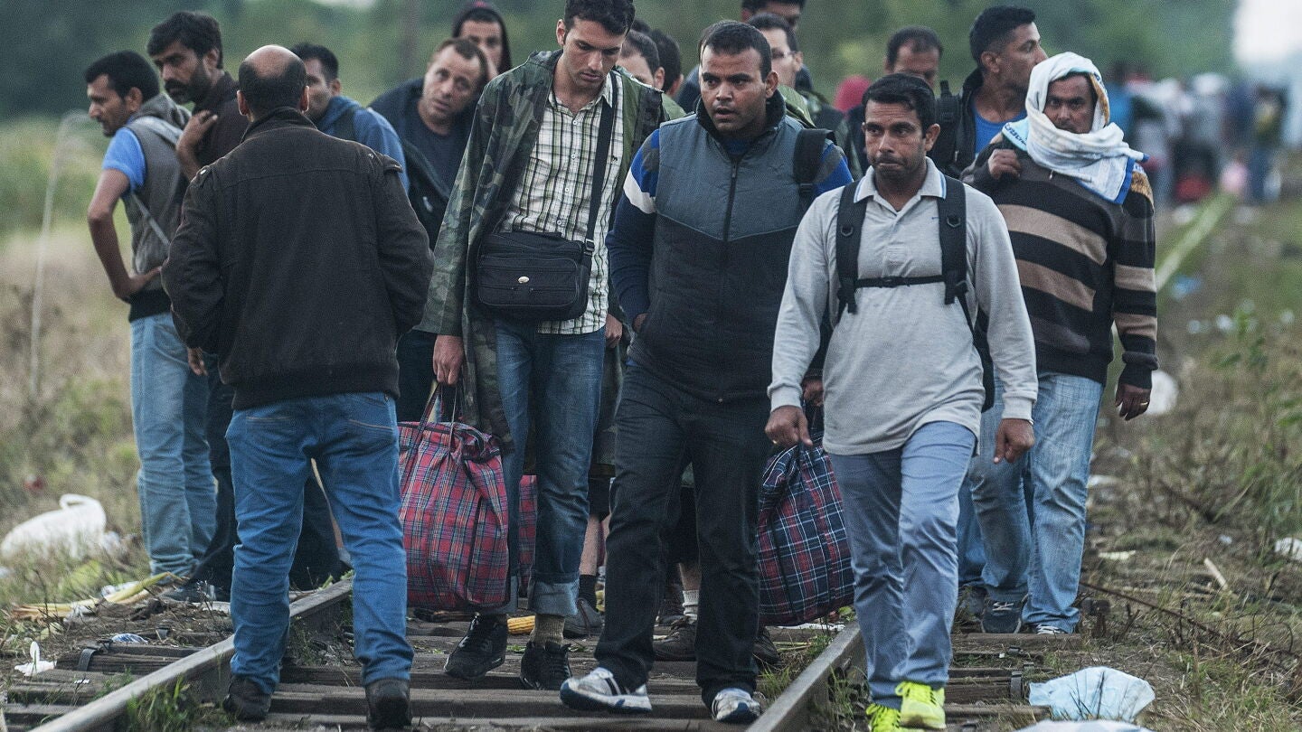 Inmigrantes caminan sobre las v&iacute;as de un tren