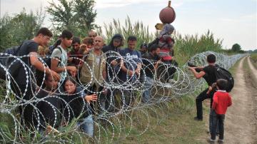 Varios refugiados sirios intentando saltar la alambrada de la frontera entre Hungría y Serbia