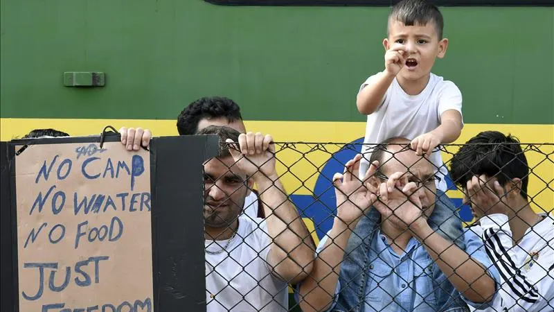 Refugiados resisten junto al tren que permanece varado hoy en la estación ferroviaria de Bicske