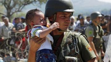 Un policía macedonio ayuda a un niño refugiado a cruzar la frontera entre Macedonia y Grecia