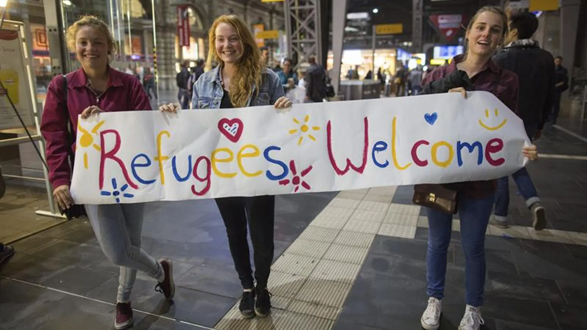 Tres voluntarias alemanas esperan con un cartel de bienvenida a los refugiados