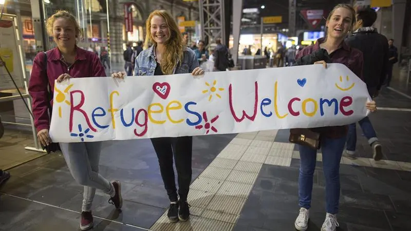 Tres voluntarias alemanas esperan con un cartel de bienvenida a los refugiados