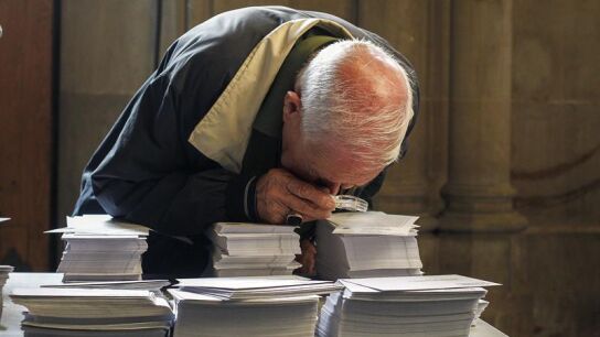Una persoma observa con una lupa las papeletas de los diferentes partidos del 27S 