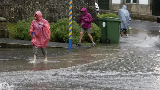 Varias personas intentan cruzar una calle anegada de agua Varias personas intentan cruzar una calle anegada de agua