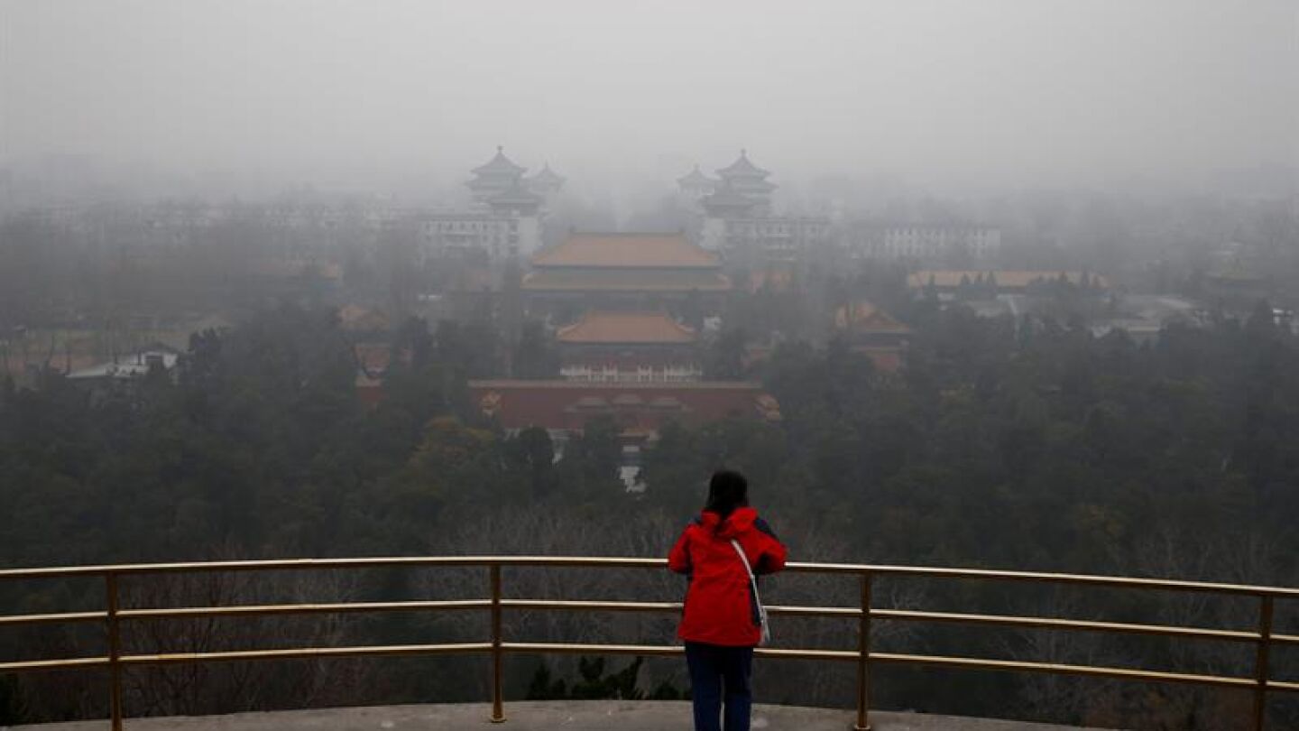 Una mujer observa el paisaje envuelto por una espesa niebla en Pek&iacute;n