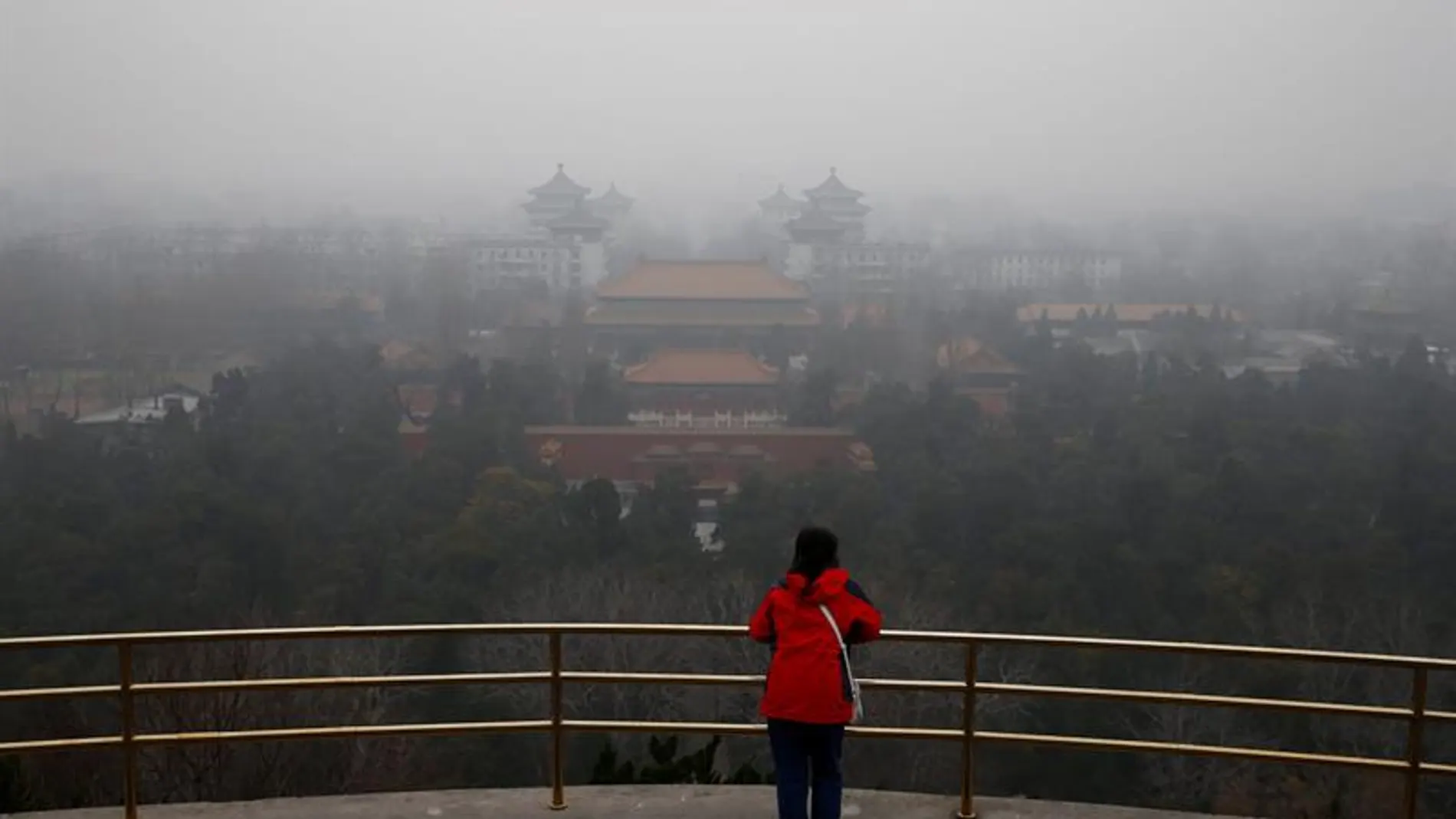 Una mujer observa el paisaje envuelto por una espesa niebla en Pekín