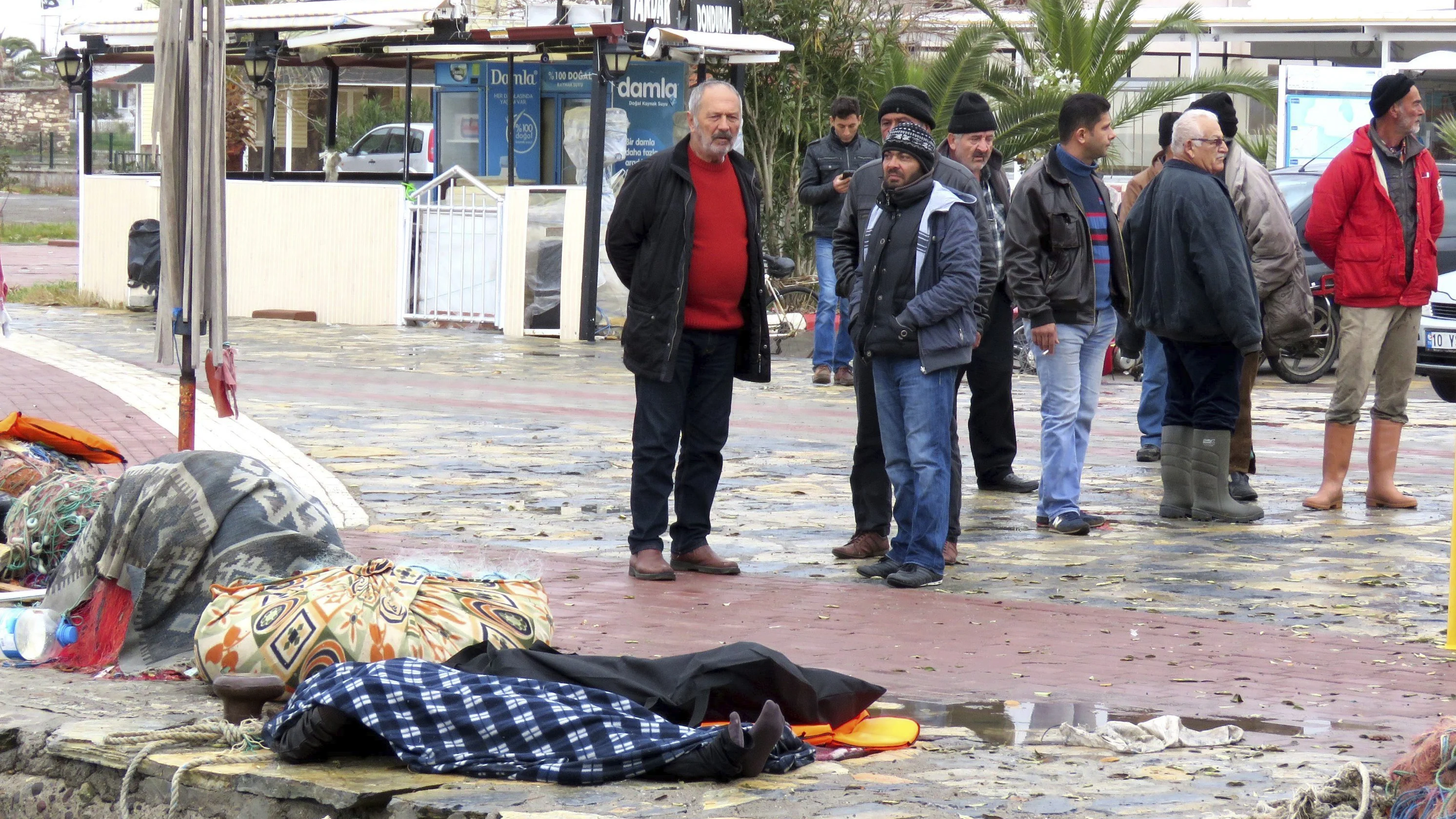 Varios curiosos permanecen cerca de varias víctimas ahogadas tras naufragar la embarcación