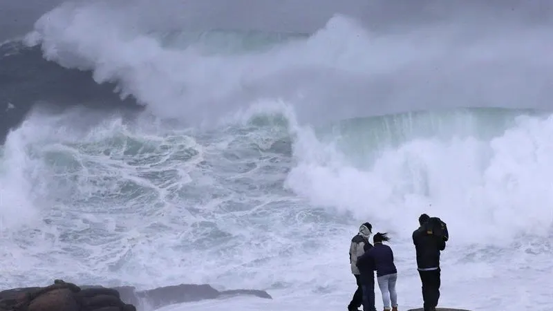 Varios turistas observan las olas en la costa esta tarde en Muxía