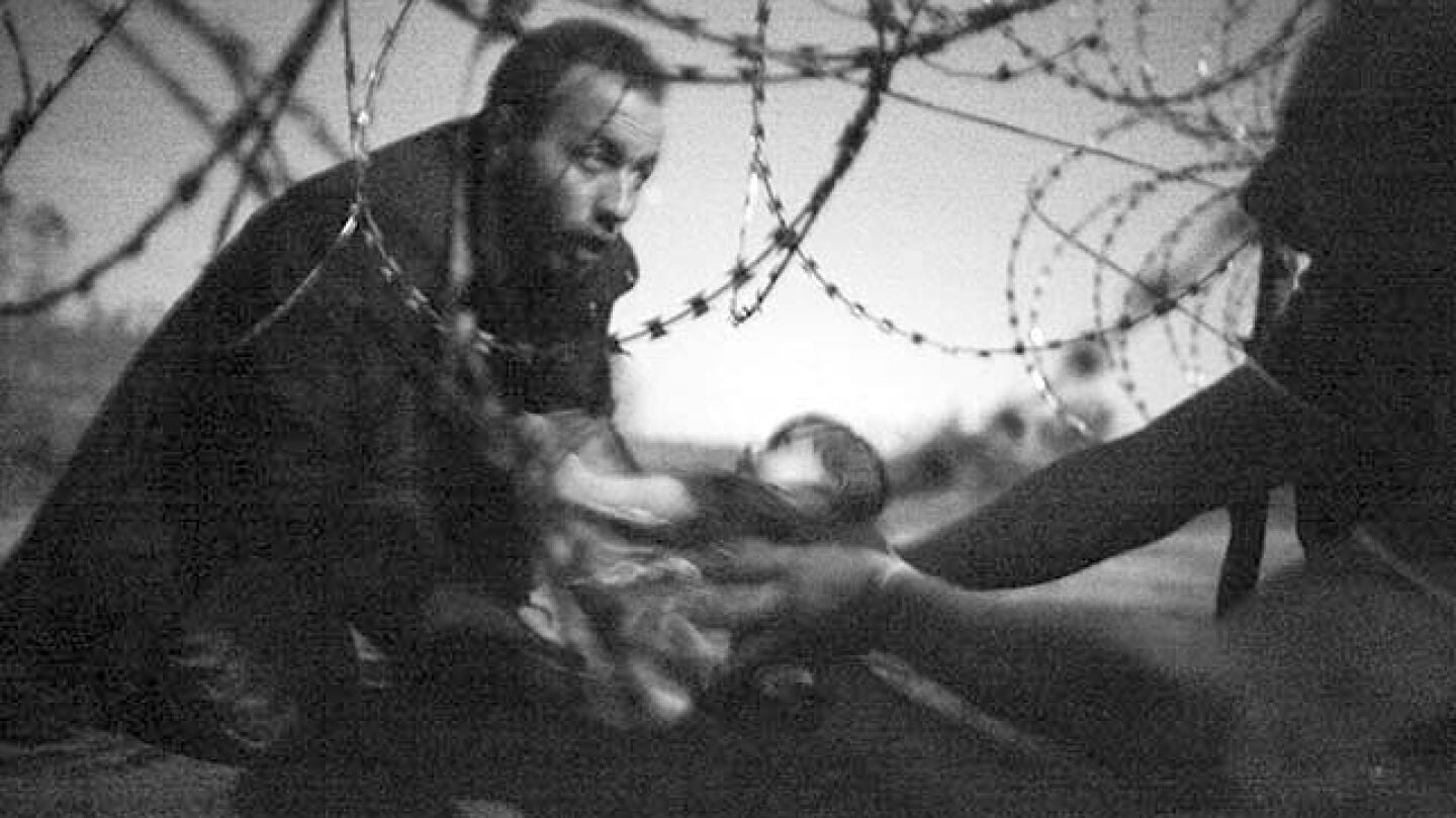 Unos refugiados pasan a un beb&eacute; por la frontera entre Serbia y Hungr&iacute;a