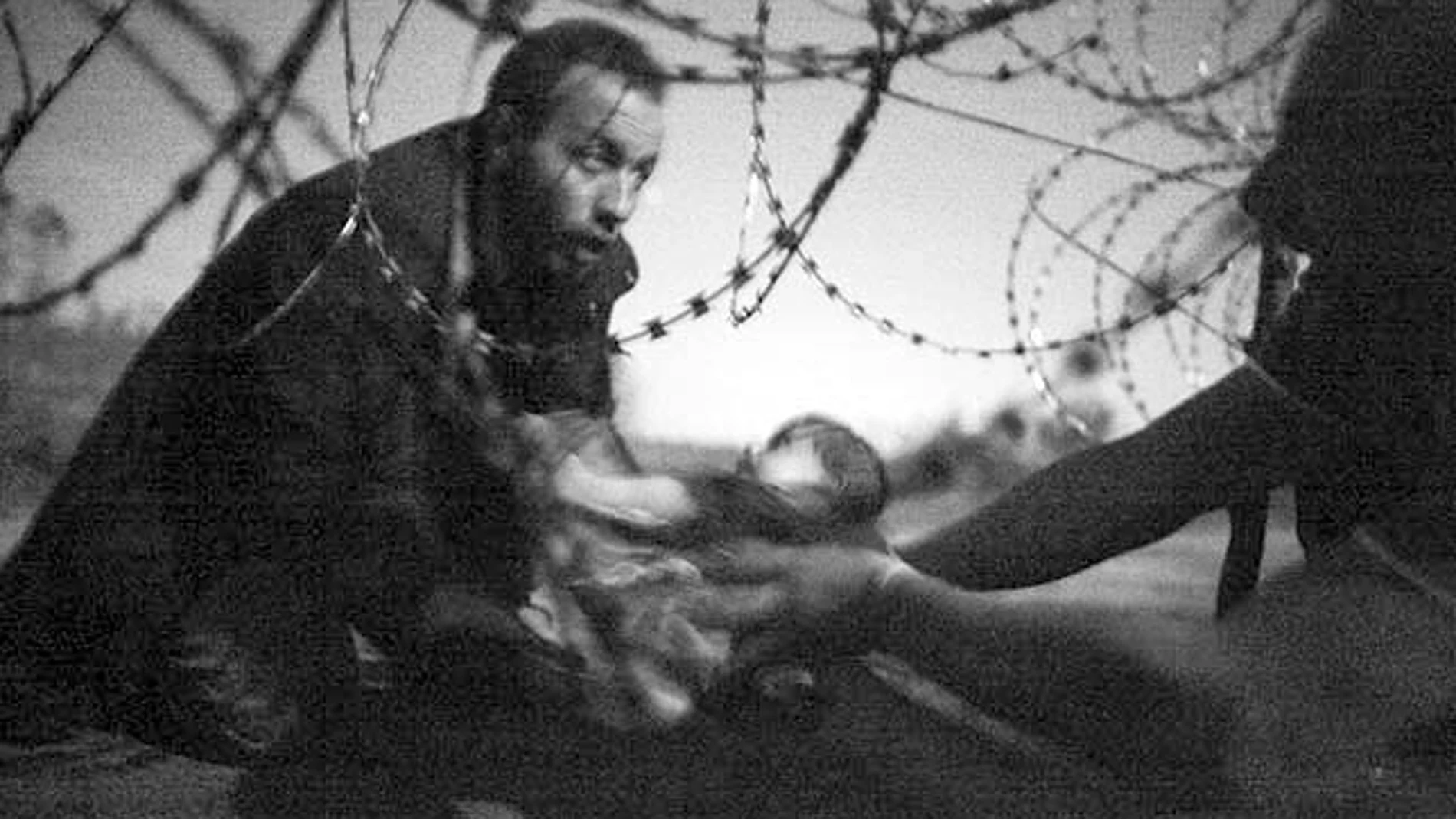 Unos refugiados pasan a un bebé por la frontera entre Serbia y Hungría