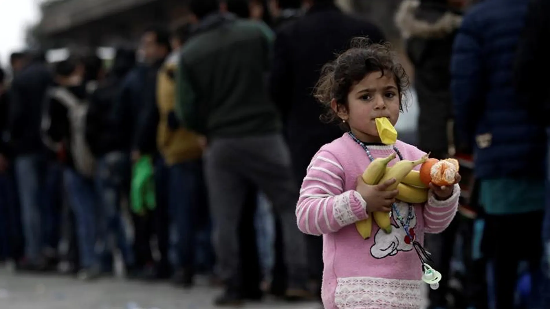 Una niña camina con fruta en las manos mientras muchos otros refugiados esperan comida