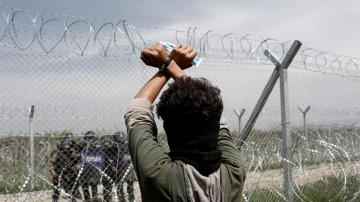 Un refugiado permanece tras la valla fronteriza frente a un grupo de policías macedonios 