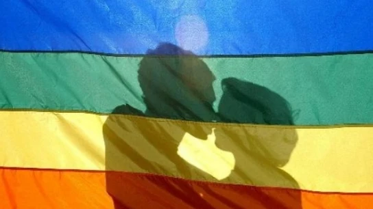 Dos jóvenes se besan tras la bandera LGTB Dos jóvenes se besan tras la bandera LGTB