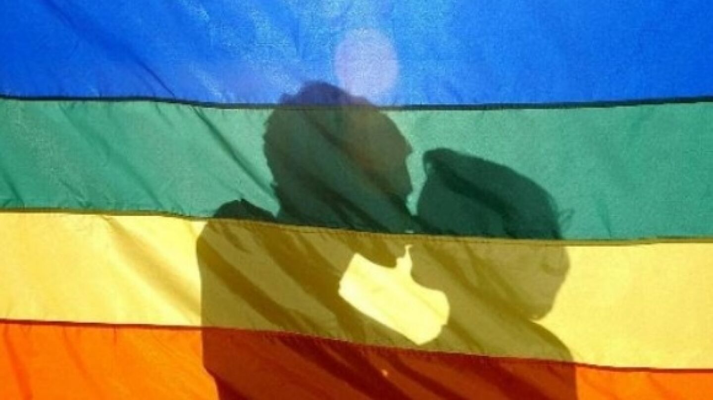 Dos j&oacute;venes se besan tras la bandera LGTB