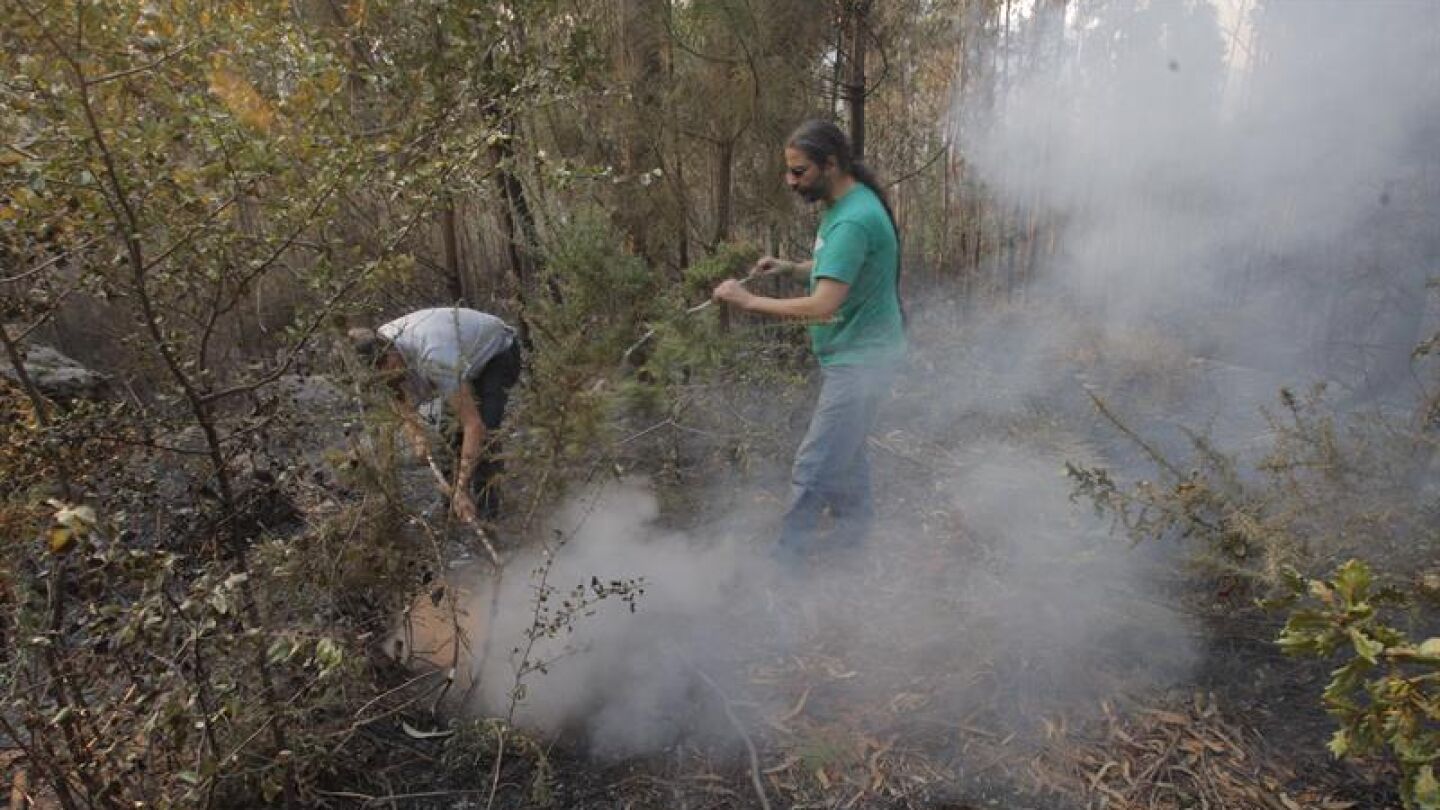 Dos vecinos intentan sofocar un foco del incendio que afecta al municipio coru&ntilde;&eacute;s de Porto Do San