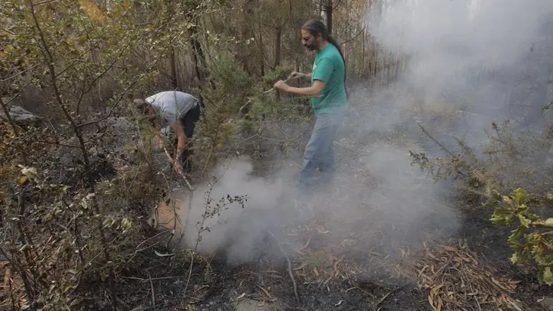 Dos vecinos intentan sofocar un foco del incendio que afecta al municipio coruñés de Porto Do San