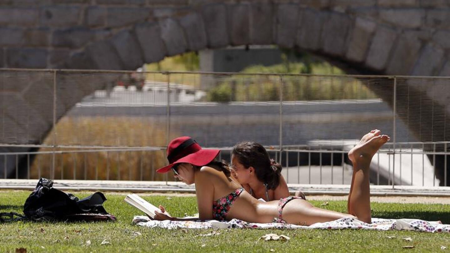 Dos personas toman el sol en las inmediaciones del parque de Madrid R&iacute;o