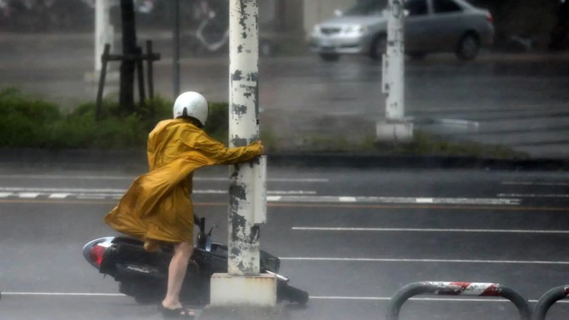 Una motorista se agarra a un poste para evitar ser arrastrada por las fuertes rachas de viento provocadas por el supertifón Meranto