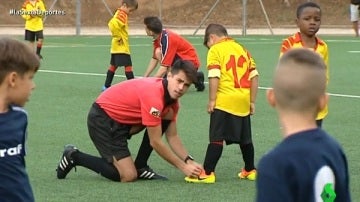 Un árbitro ayuda a un niño a atarse la bota