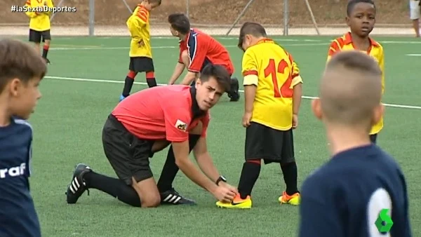 Un árbitro ayuda a un niño a atarse la bota