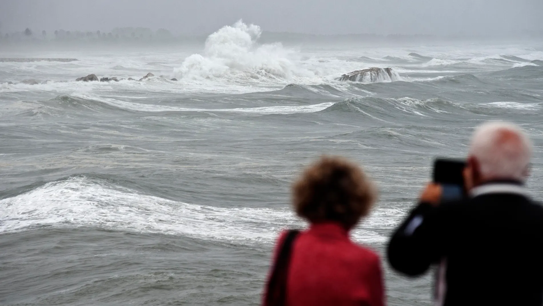 Unos vecinos toman imágenes en una playa afectada por un fuerte temporal.